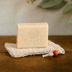 Australian-made Tilley Goats Milk & Manuka Honey Soap resting on Luxe & Humble’s Purity Pouch, handcrafted from natural sisal with a wooden bead detail. Captured on a timber surface beneath soft greenery — reflecting slow living, sustainability, and handmade Australian craft.