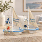 Two miniature wooden sailboat ornaments in blue and white with Life Is A Journey canvas sails, displayed on a stone tabletop.
