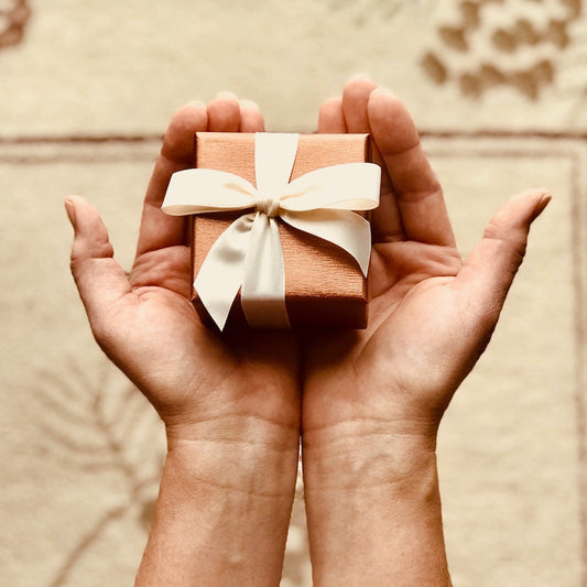Hands Holding a Rose Gold gift box with a bow.  To signify Luxe & Humble Digital Gift Vouchers.